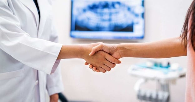 A dentist shaking hands with a new associate in front of an x-ray