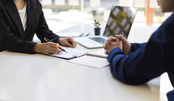 One set of hands folded on a desk with the other set taking notes